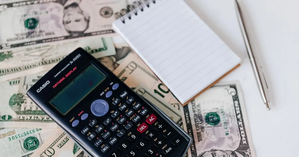 A calculator resting on banknotes beside a notepad